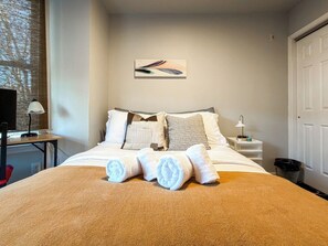 A neatly made bed with rolled towels, a bedside table with a lamp, and a wall-mounted artwork. - Private Studio Near Upenn & Drexel (Philadelphia)