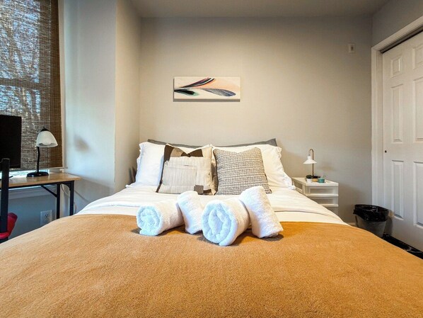 Una cama bien hecha con toallas enrolladas, una mesita de noche con lámpara y una obra de arte en la pared.