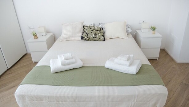 A neatly made bed with white linens and a green throw blanket, two white towels on the bed, and two bedside tables with lamps and small plants. - Rome Urban Retreat - ChiacchioProperty (Rome)