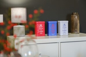 Ein weißer Tisch mit einer gefrosteten Lampe, drei mit 'KEEP CALM and CARRY ON' beschriftete Boxen und einer hohen, gerippten Vase.
