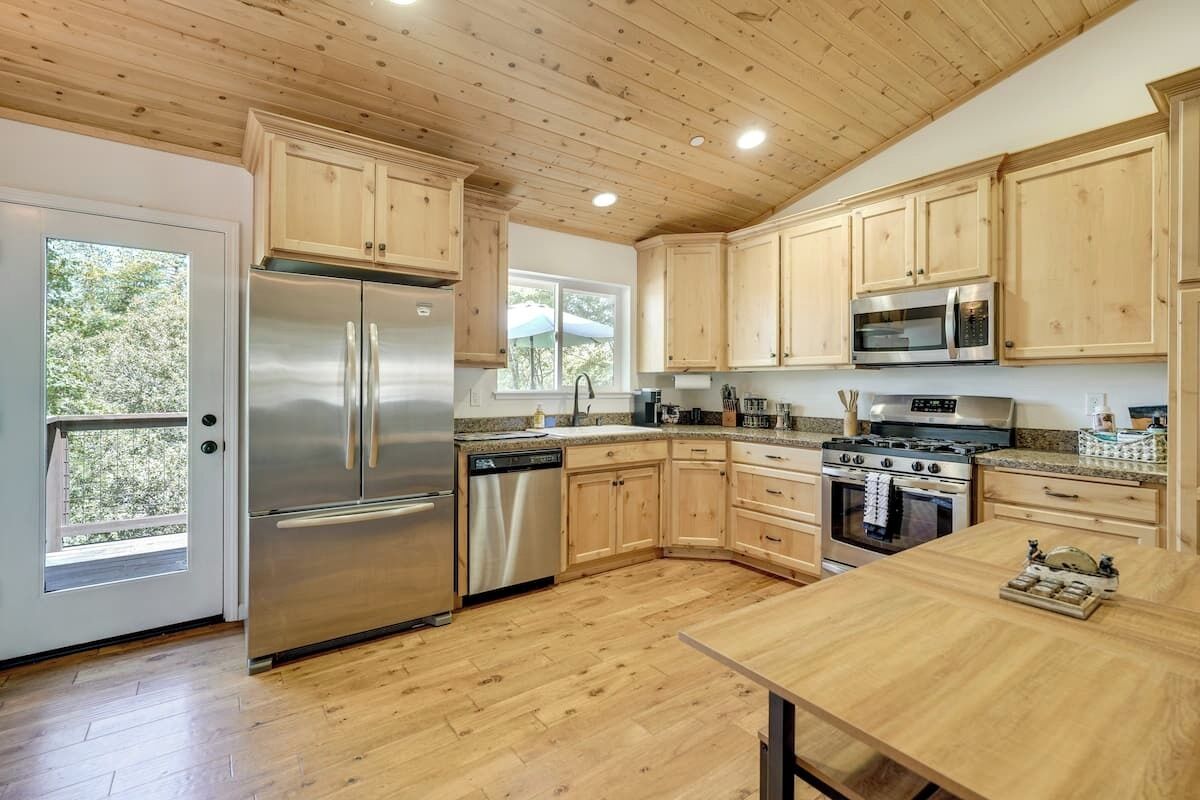 A modern kitchen with wooden cabinets, stainless steel appliances, and a large window.