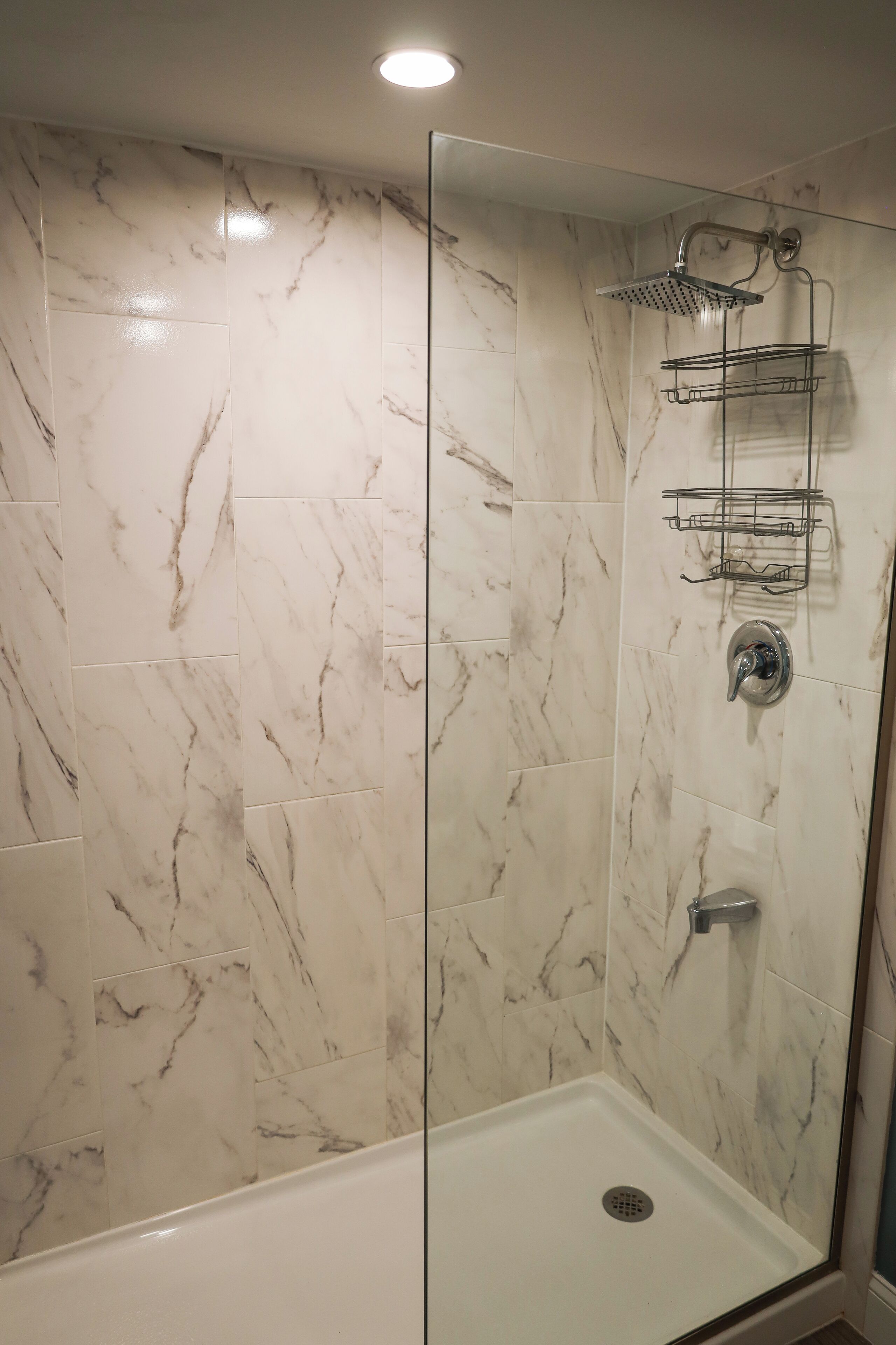 A glass-enclosed shower with a handheld showerhead and a wall-mounted towel rack.