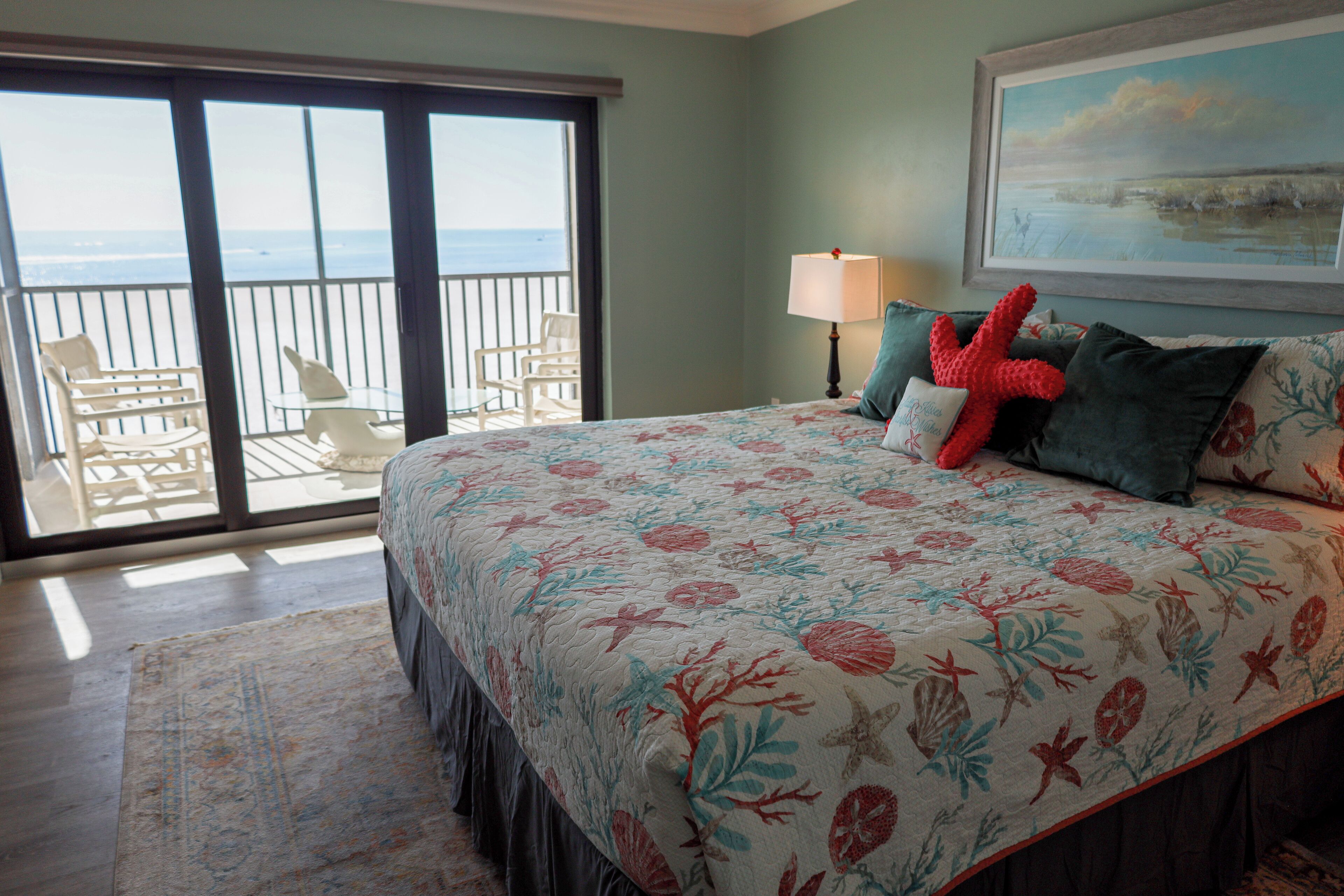 A bedroom with a large bed, a balcony with chairs, and a painting on the wall.