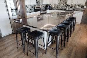 A kitchen with a large island, stainless steel appliances, and black bar stools. - Luxury Fort Myers Beach Penthouse - Stunning Beachfront View & Pool (Fort Myers Beach)