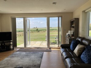A living room with a large sliding glass door leading to a patio, a leather sofa, a television, and a bookshelf. - Seadrift (Norwich)