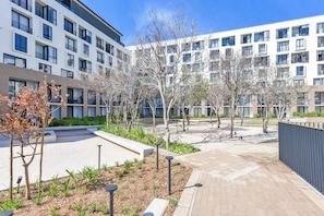 A modern building with multiple floors, outdoor seating areas, and a landscaped courtyard with trees and plants. - One Rosebank | Rustic Luxe 2BR Haven (Johannesburg)