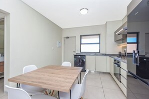 A compact kitchen with a wooden table and white chairs, a built-in oven, and a washing machine. - Effortless Luxury Living at The View (Sandton)