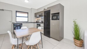 A modern kitchen with a wooden table and white chairs, stainless steel appliances, and a potted plant. - Effortless Luxury Living at The View (Sandton)