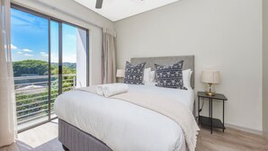 A bedroom with a large bed, a ceiling fan, a nightstand, and a view of greenery through a sliding glass door. - Effortless Luxury Living at The View (Sandton)