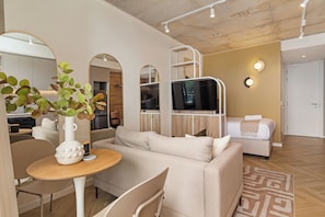 A modern living room with a sofa, a dining table with a vase, and a mirror. - Central Sea Point Studio | Rooftop Pool (Cape Town)