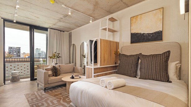 A modern hotel room with a large bed, a sofa, a TV, and a city view. - Central Sea Point Studio | Rooftop Pool (Cape Town)