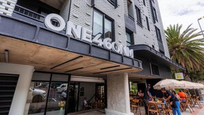 A building with a sign reading "ONE 460M" and outdoor seating with umbrellas. - Central Sea Point Studio | Rooftop Pool (Cape Town)