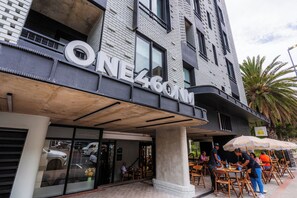 A building with a sign reading "ONE 460M" and outdoor seating with umbrellas. - Central Sea Point Studio | Rooftop Pool (Cape Town)