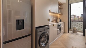 A modern kitchen with a built-in washer and dryer, wooden cabinets, and a view of the city through a large window. - Central Sea Point Studio | Rooftop Pool (Cape Town)