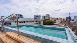 A rooftop swimming pool with a wooden deck and a cityscape in the background. - Central Sea Point Studio | Rooftop Pool (Cape Town)