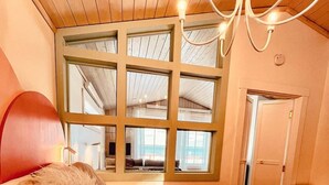 Ein Schlafzimmer mit großem Fenster, einem Bett mit flauschigem Kopfkissen, einem Holz-Kopfteil und einem Tablett mit zwei Tassen.