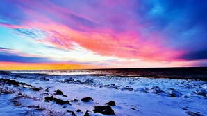 Ein verschneiter Strand mit einem farbenprächtigen Sonnenuntergangshimmel.