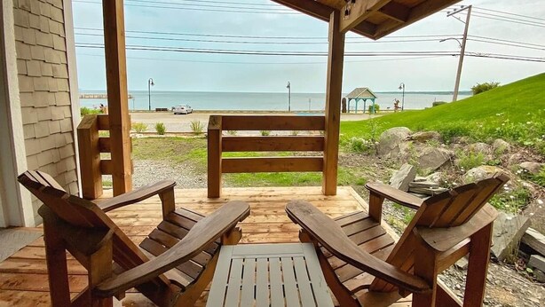 Eine Holzterrasse mit zwei Adirondack-Stühlen, die Blick auf das Meer bietet.