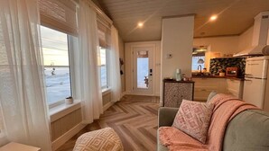 Ein gemütliches Wohnzimmer mit einer Couch, einem Hocker und Blick ins Freie durch große Fenster.