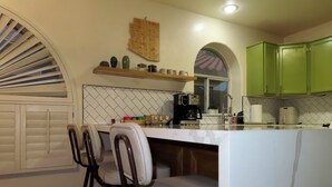 Una cocina con barra, taburetes, cafetera y armarios verdes.