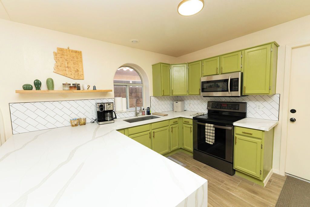 A kitchen with green cabinets, a white countertop, and a black oven.