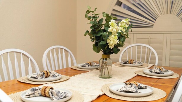 Una mesa de comedor dispuesta con platos, servilletas y un jarrón de flores.