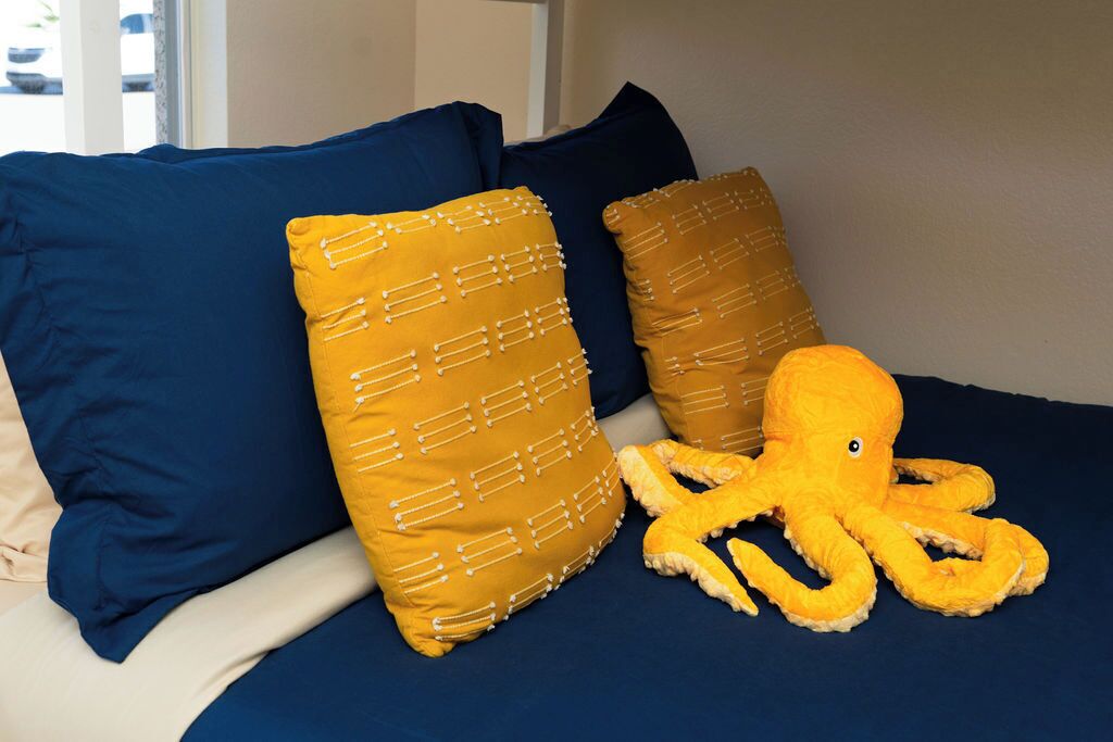 A bed with blue and mustard pillows and a plush octopus toy.