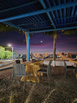 An outdoor seating area with tables and chairs, a hammock, and a view of the night sky.