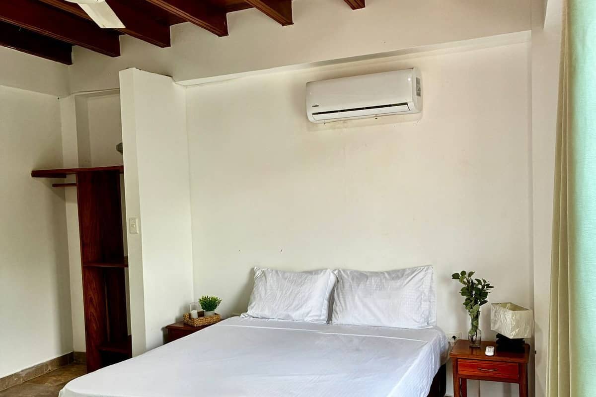 A bedroom with a bed, wooden floor, ceiling fan, and an air conditioning unit.