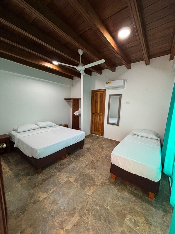 A room with two beds, a ceiling fan, an air conditioning unit, and a wooden door.