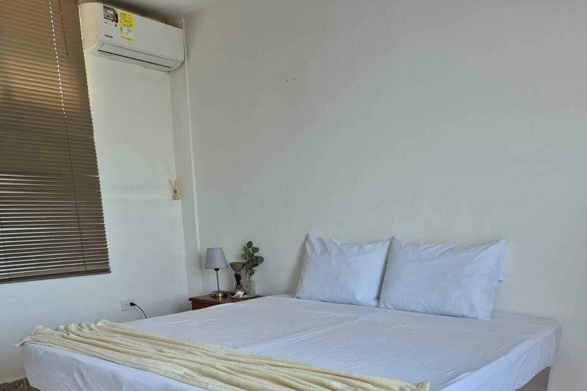 A single-bed room with a patterned floor, a bedside table with a lamp, and a wall-mounted air conditioner.