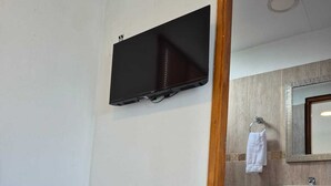 Habitación de hotel con cama, televisor de pantalla plana en la pared, lavabo y espejo.