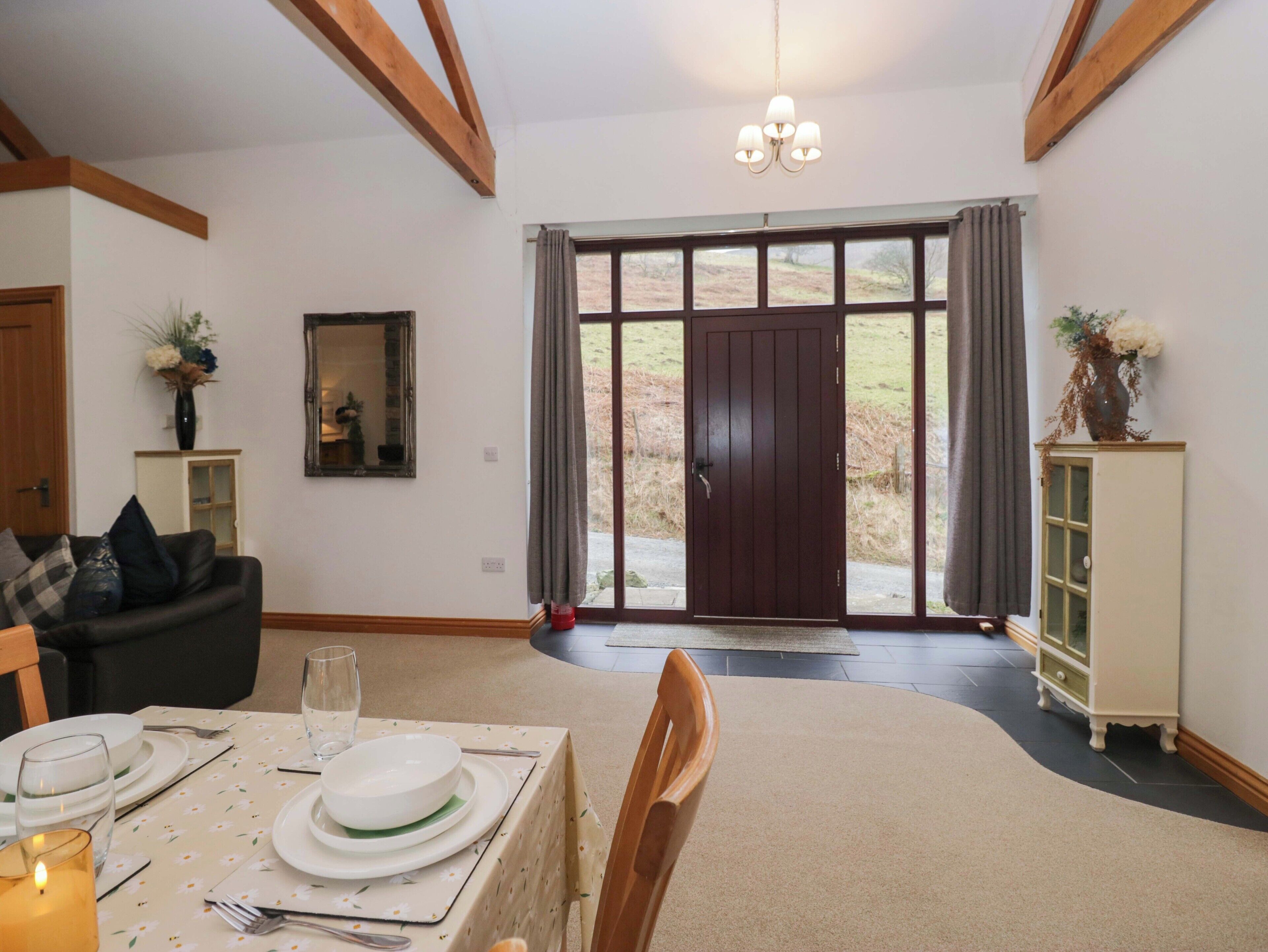 A dining area with a table set for four, a sofa, a cabinet, and a large window with curtains.