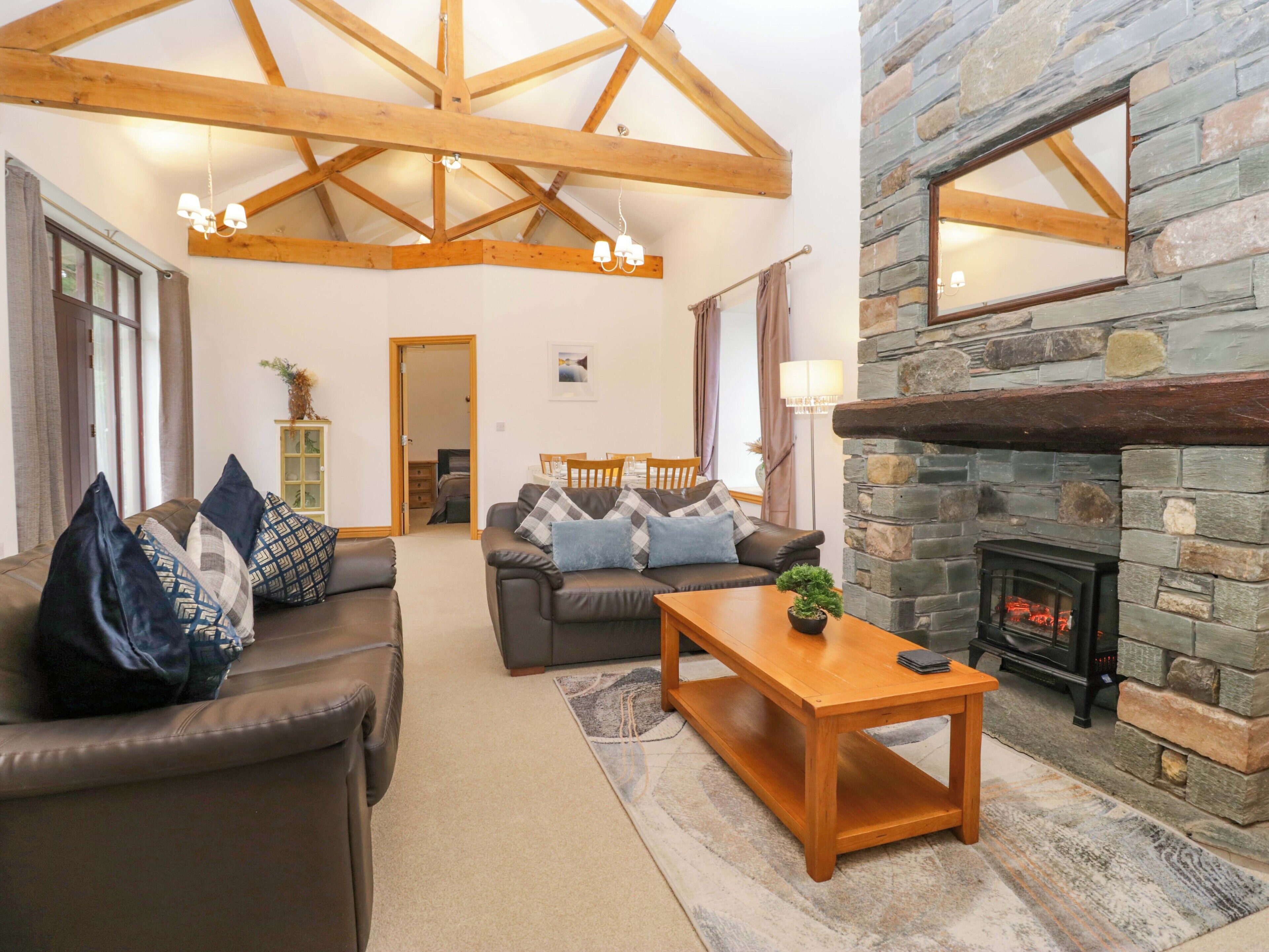 A cozy living room with a stone fireplace, leather sofas, and a wooden ceiling.