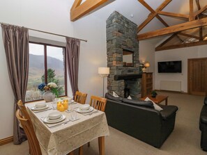 A dining area with a table set for four, a stone fireplace, and a sofa in the background. - Newlands Fell Cottage (Keswick)