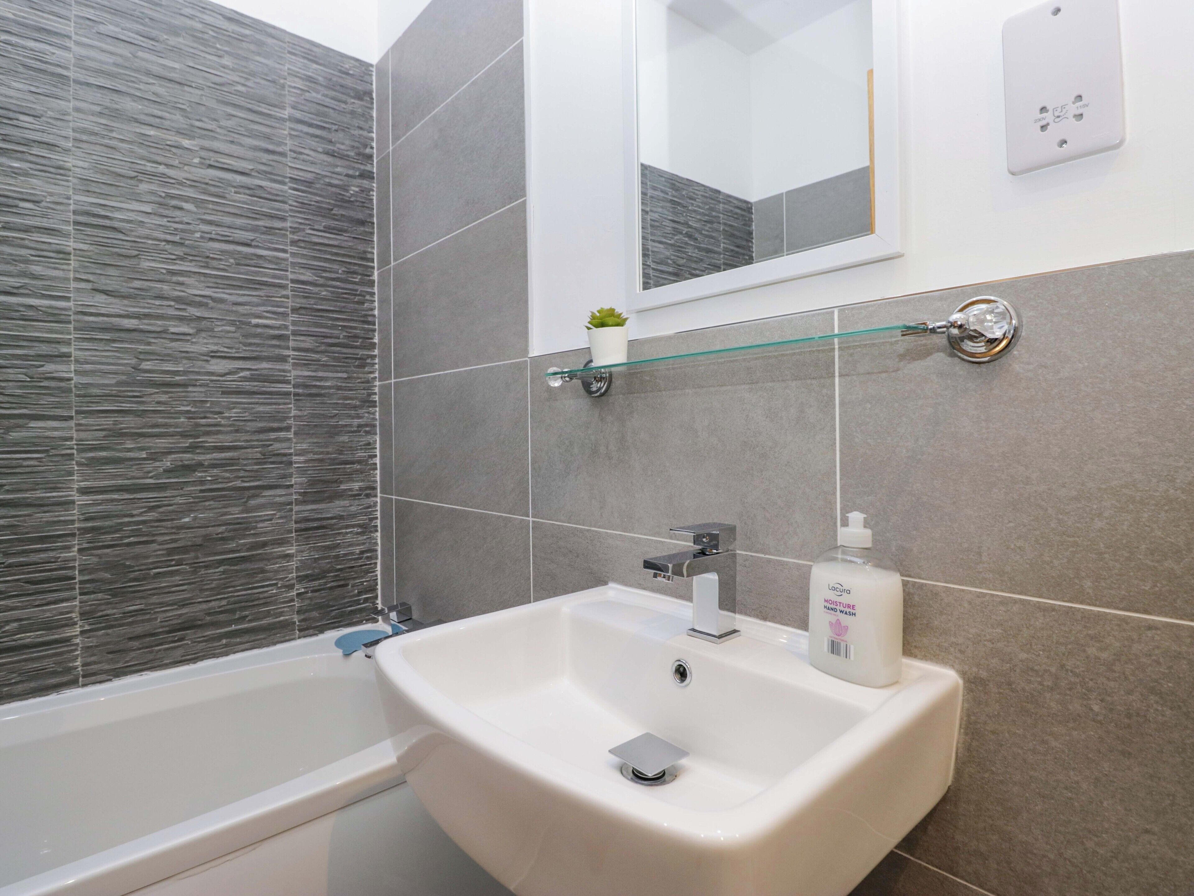 A modern bathroom with a white sink, a glass shelf, and a mirror.