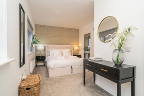 Une chambre à coucher moderne avec un grand lit, des tables de chevet, une commode, un miroir et un vase rempli de fleurs.