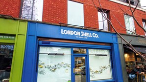 Fachada azul y verde con un letrero que dice 'LONDON SHELL CO.' y un amplio ventanal que muestra un restaurante de pescados y una tienda de vinos.