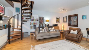 Una sala de estar moderna con una escalera espiral, un sofá, un sillón de cuero, una estantería y una lámpara.