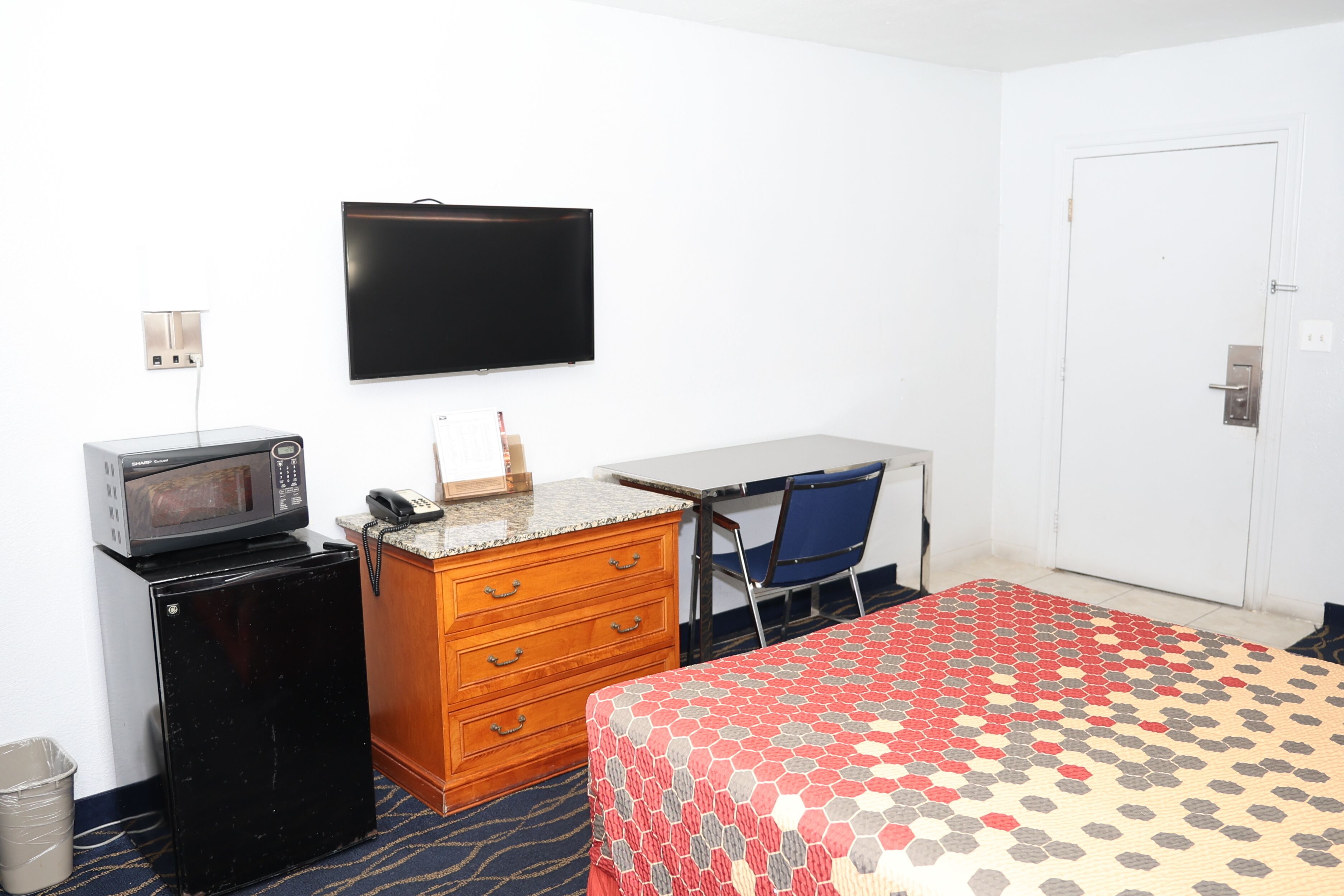 Une chambre d’hôtel équipée d’un lit, d’un bureau, d’une chaise, d’une télévision, d’un four à micro-ondes et d’un petit réfrigérateur.