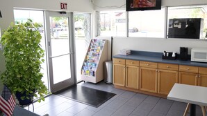 A reception area with a plant, a magazine rack, a microwave, and wooden cabinets.
