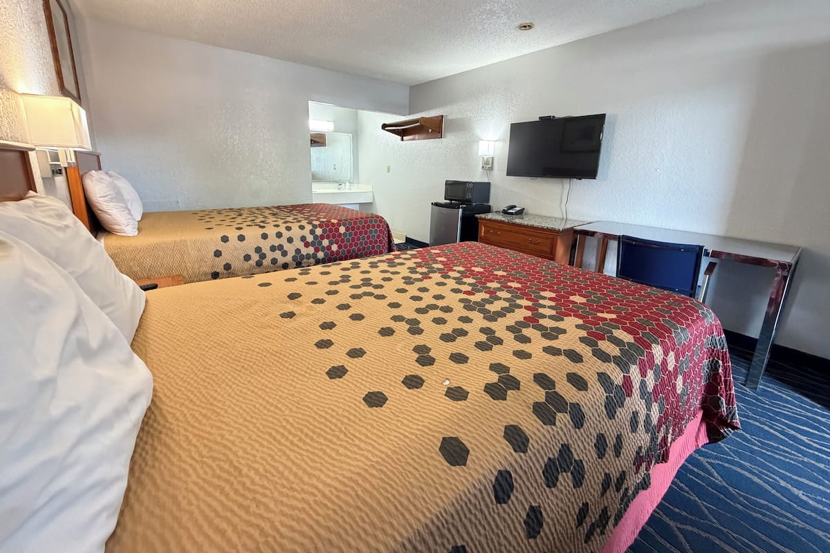 A hotel room with two beds, a desk, a TV, and a mirror.
