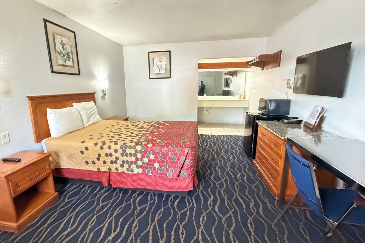 A hotel room with a bed, a desk, a television, and a bathroom visible through an open door.