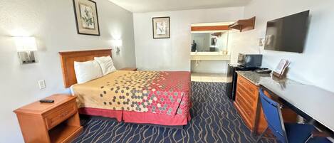 A hotel room with a bed, a desk, a television, and a bathroom visible through an open door.