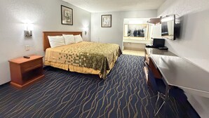 A hotel room with a bed, bedside table, lamp, dresser, mirror, and wall-mounted light fixture.