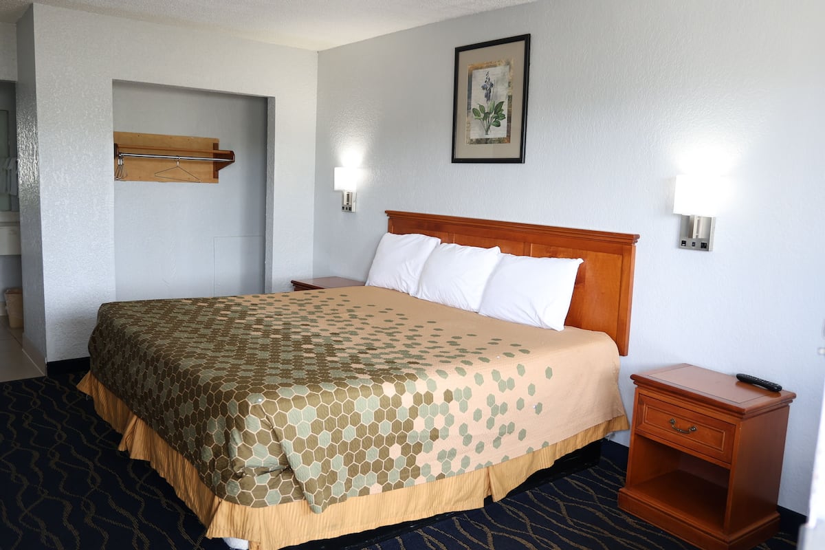 A hotel room with a bed, bedside table, lamp, and a wall-mounted shelf.