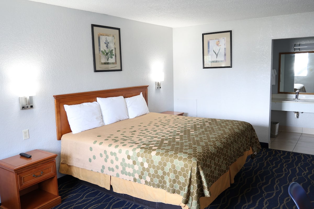 A hotel room with a bed, a nightstand, a mirror, and two framed pictures on the wall.