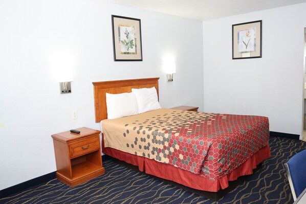 Une chambre d’hôtel avec un lit doté d’une tête de lit en bois, une table de chevet avec un tiroir, un tableau encadré au mur et une moquette à motifs.