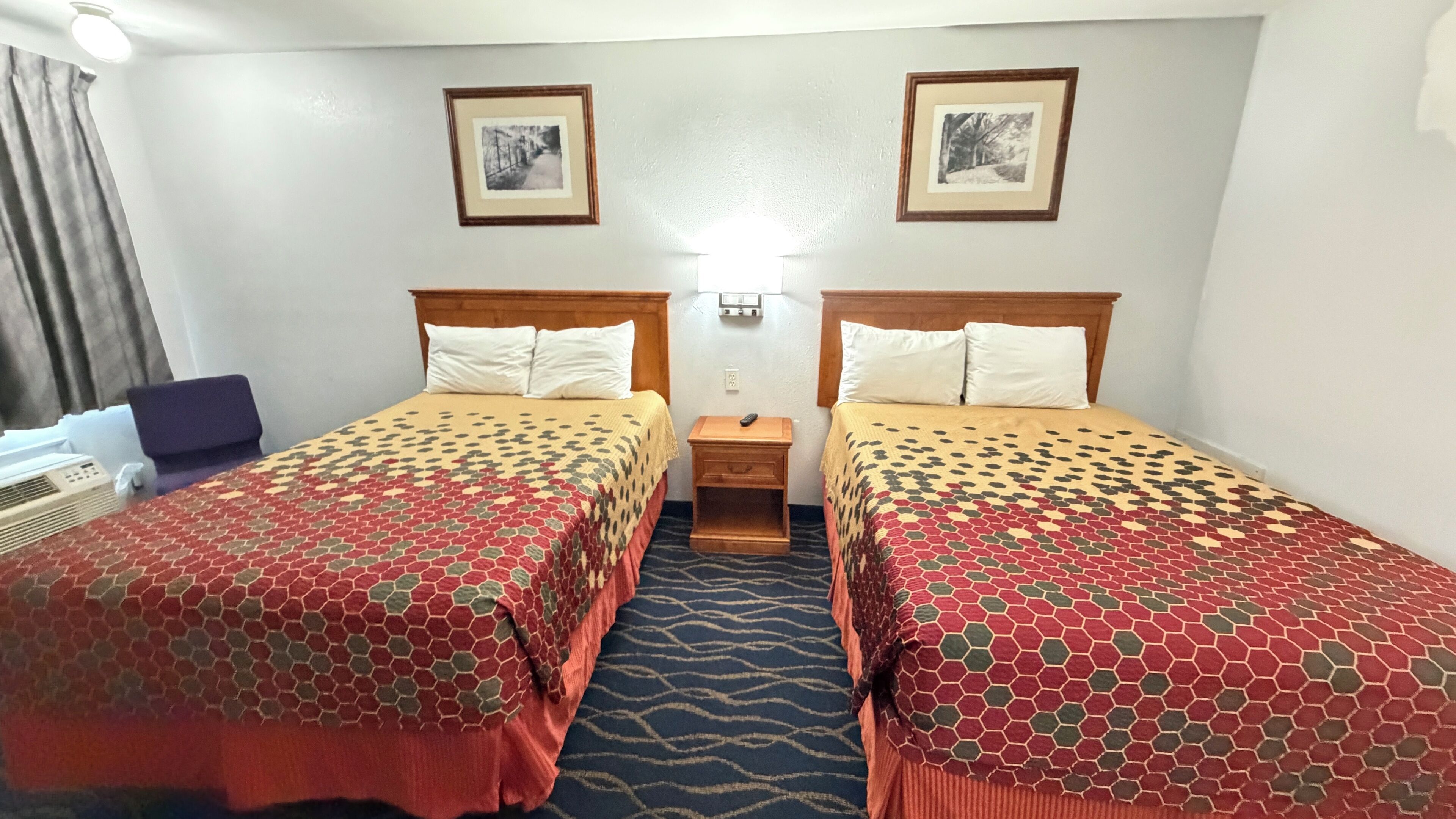 Habitación de hotel con dos camas, una mesita de noche, un escritorio y dos cuadros en la pared.