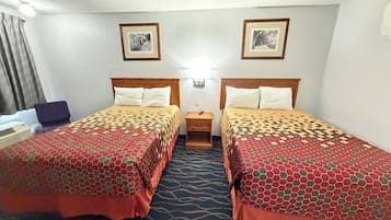 A hotel room with two beds, a nightstand, a desk, and two framed pictures on the wall.